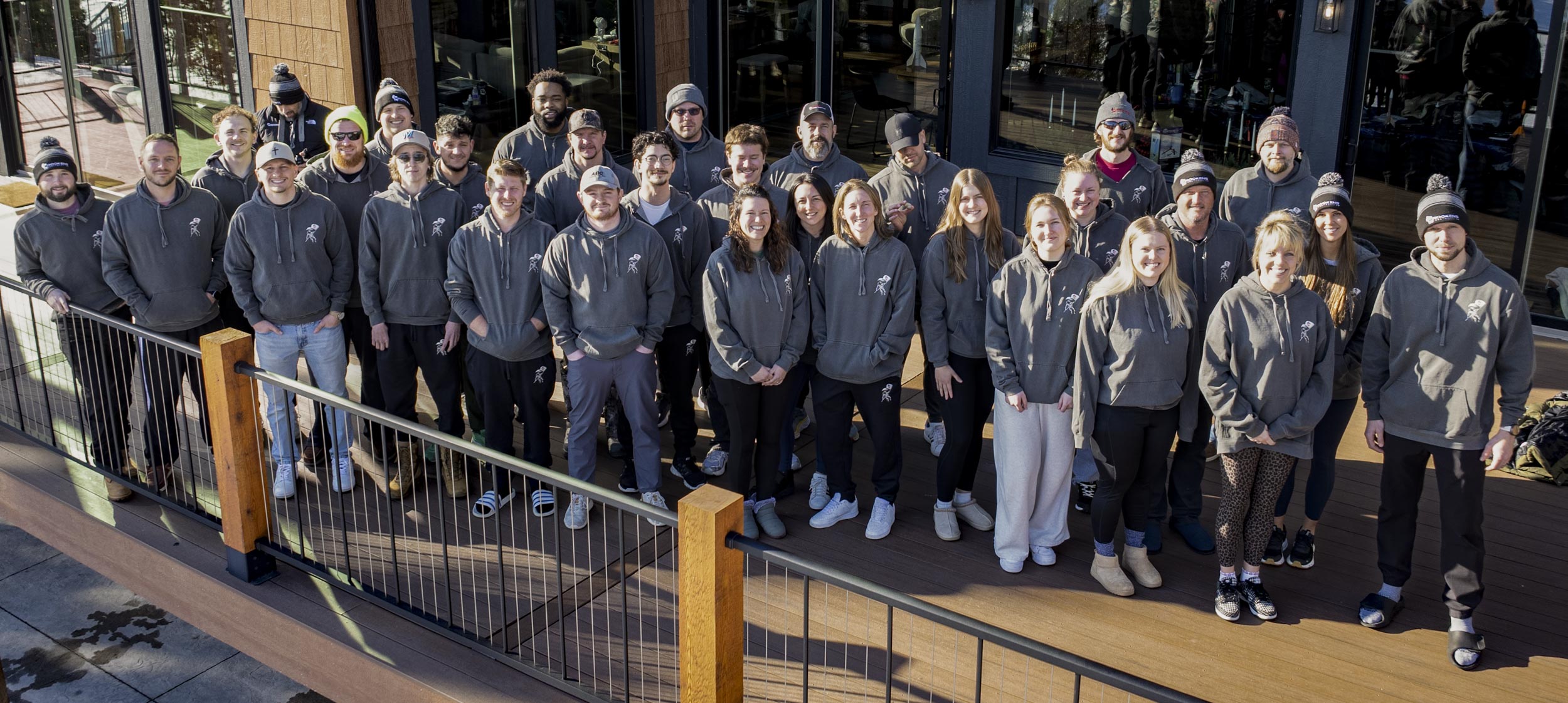35 adults stand together posing for the camera on a wide porch with a front railing.